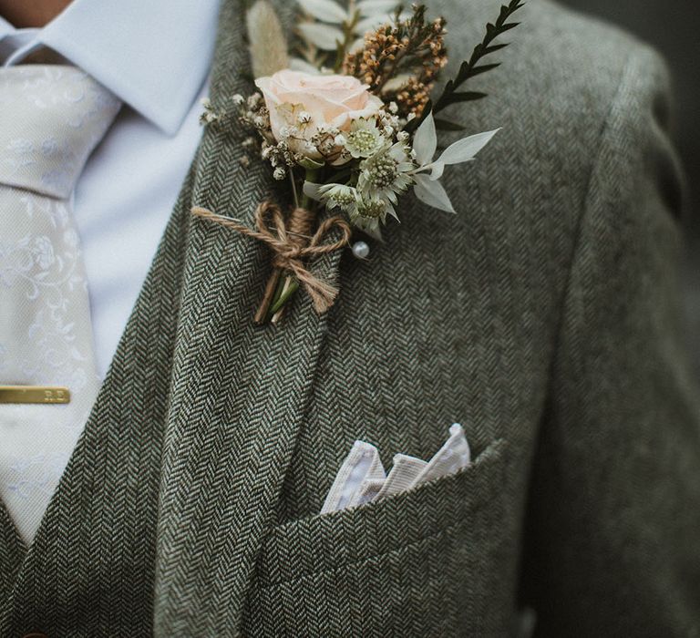 Groom wears pastel rose buttonhole tied with brown string 