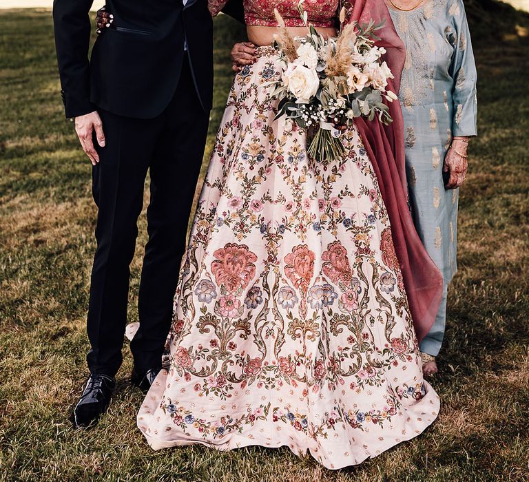 Indian bride wears traditional lehenga with floral embellishment and stands beside her groom and nan