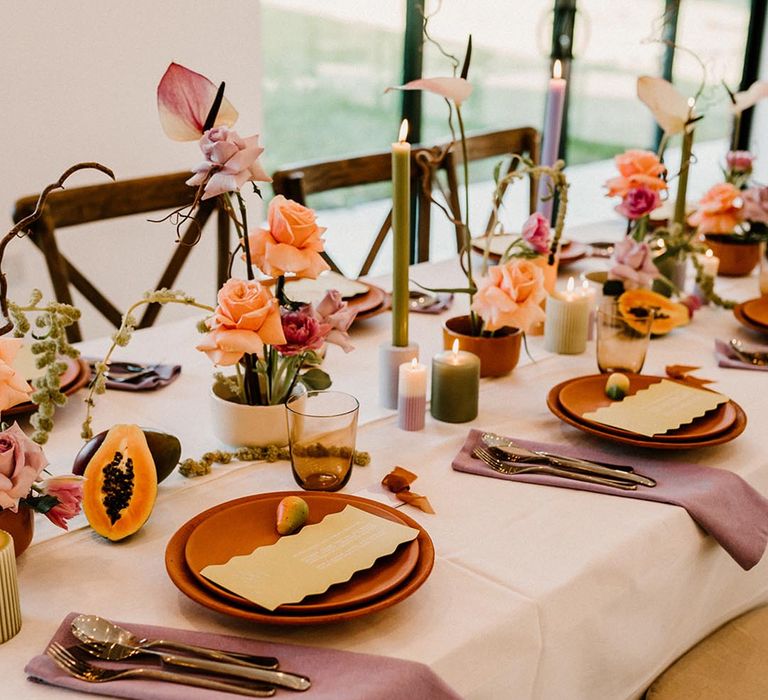 Terracotta wedding plates with lavender wedding napkins, fruit decor, and green and purple candles 