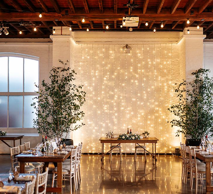 Sweetheart table in front of fairy light curtain in rustic styled venue at Trinity Buoy Wharf 