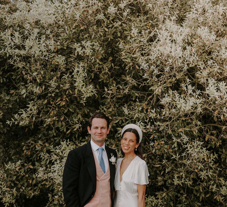 Groom in black suit with pink waistcoat and blue tie with pinstriped trousers with the bride in a Ghost satin wedding dress with buttons 