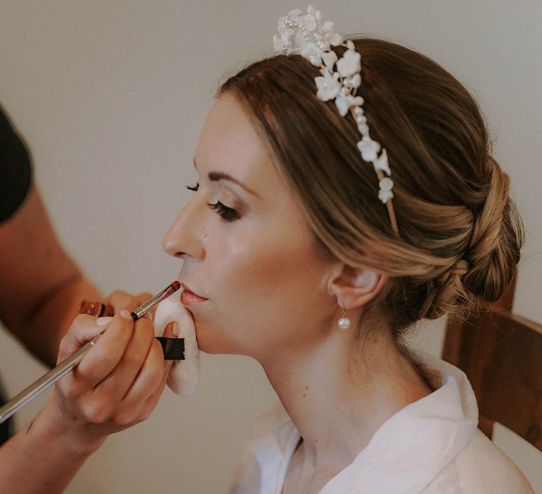 Bride wearing a white flower pearl wedding headband siting as she gets her makeup done 