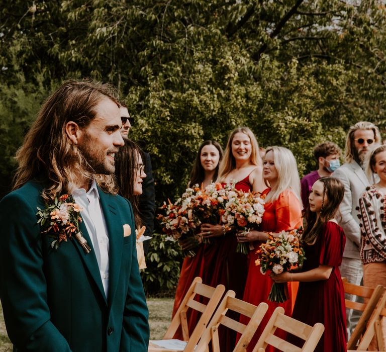 Groom wears green suit with colourful floral buttonhole 