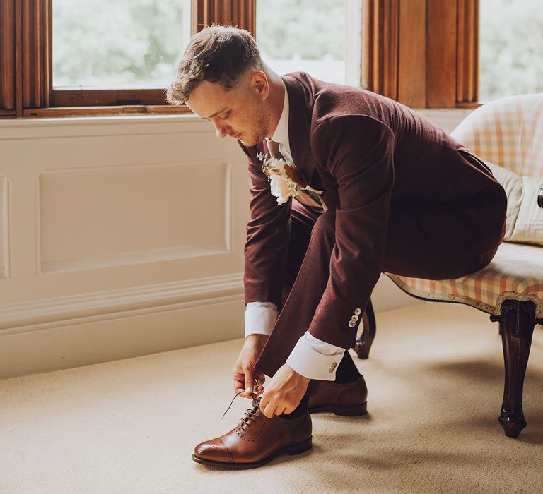 Groom wears maroon suit complete with brown brogues and floral buttonhole 