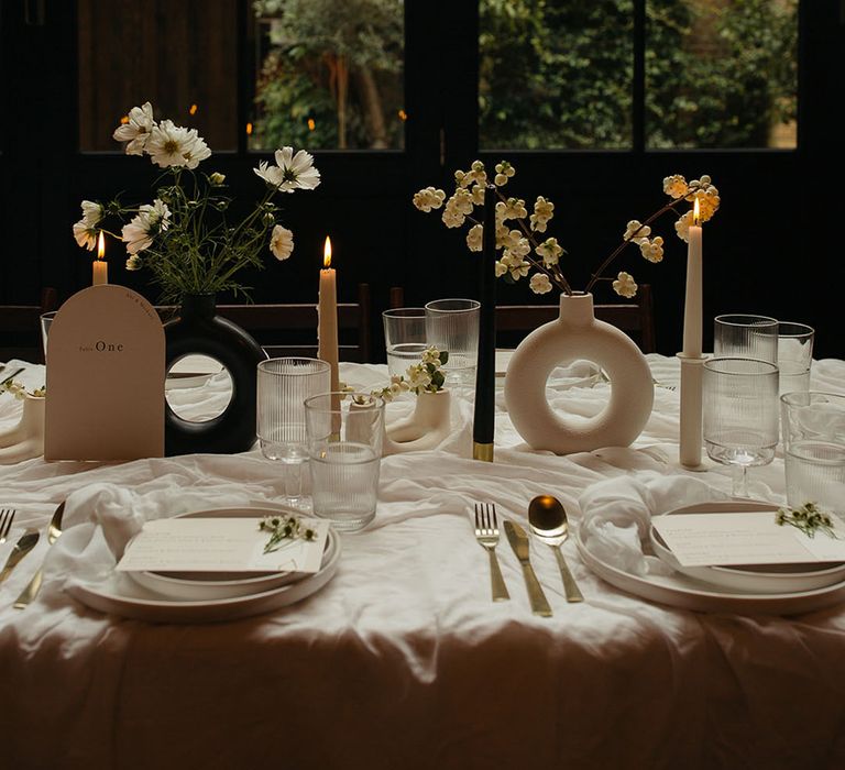 Black and white table decorations, white tablecloth circular vases, white flowers, gold cutlery and minimalistic wedding stationery