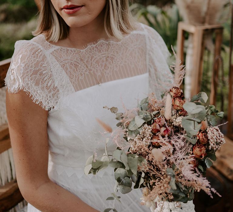 Bride wearing a sheer eyelash lace boho wedding dress and beige hat with dried flowers and cotton