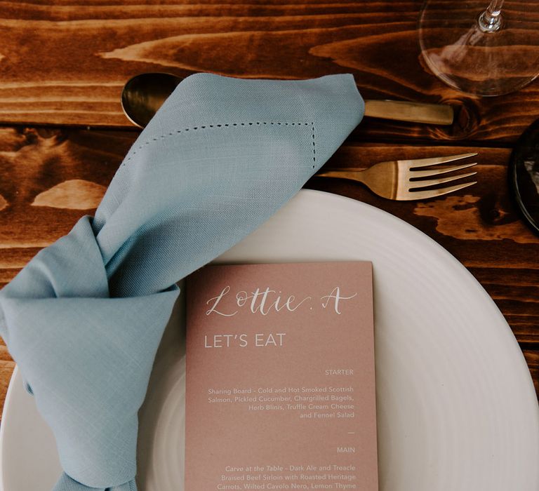 Pink wedding menu with blue napkin on white plate for pastel theme wedding reception with gold cutlery 