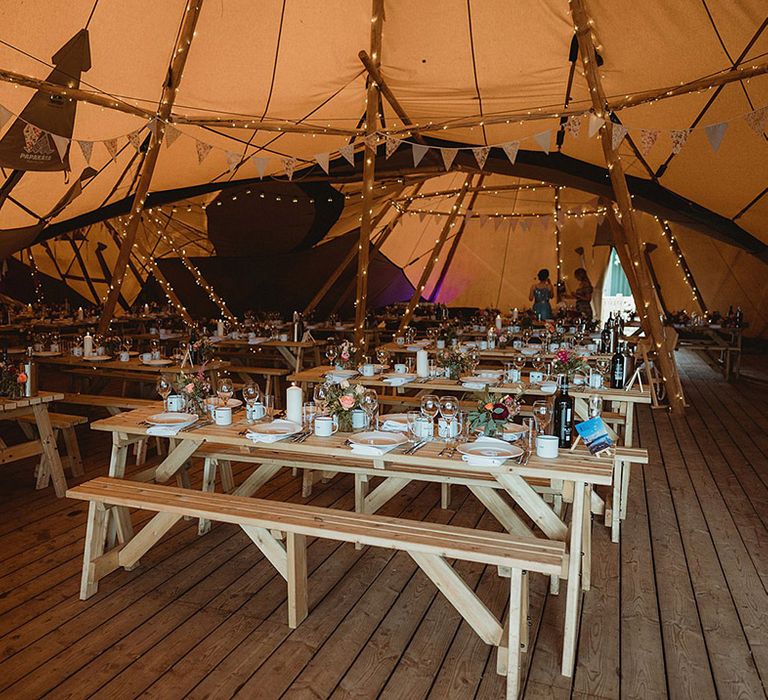 Wooden benches decorate the wedding tipi with pink roses and DIY streamer decorations 