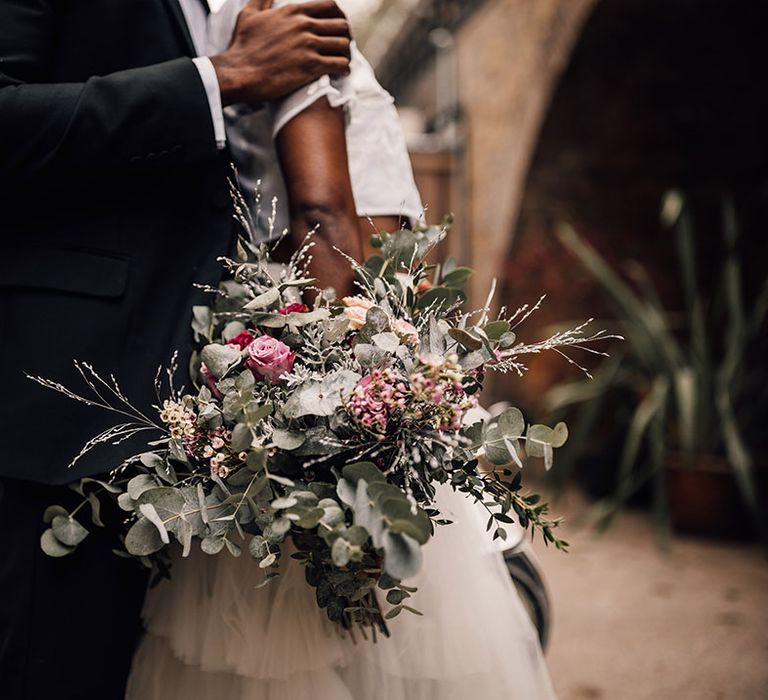 Black Bride holds a bridal bouquet featuring eucalyptus, pink roses and waxflower