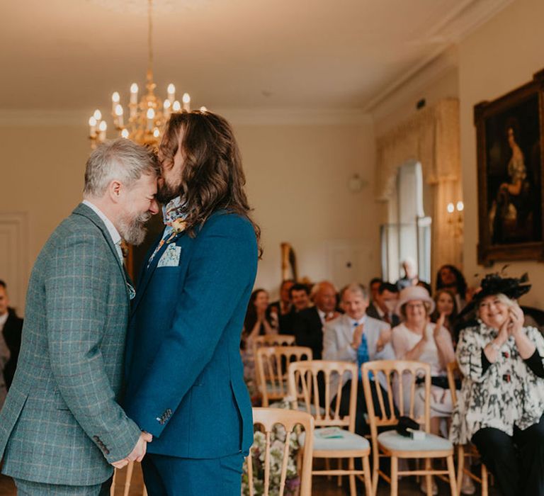 Groom with long hair kisses his groom on the forehead after wedding ceremony 