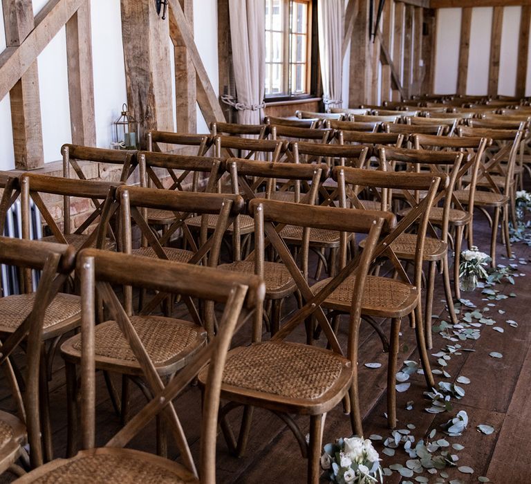 Rustic aisle decor at Gate Street Barn complete with wooden chairs and eucalyptus leaves lining the aisles alongside small white floral arrangements