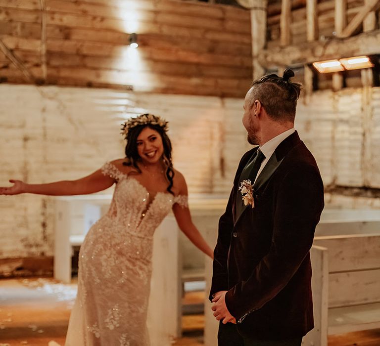 The groom in a burgundy velvet suit jacket turns around and sees the bride for the first time wearing a sparkly lace wedding dress 