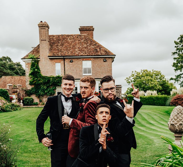 Groomsmen in black tuxedos with the groom in a burgundy suit for funny groom party shot 