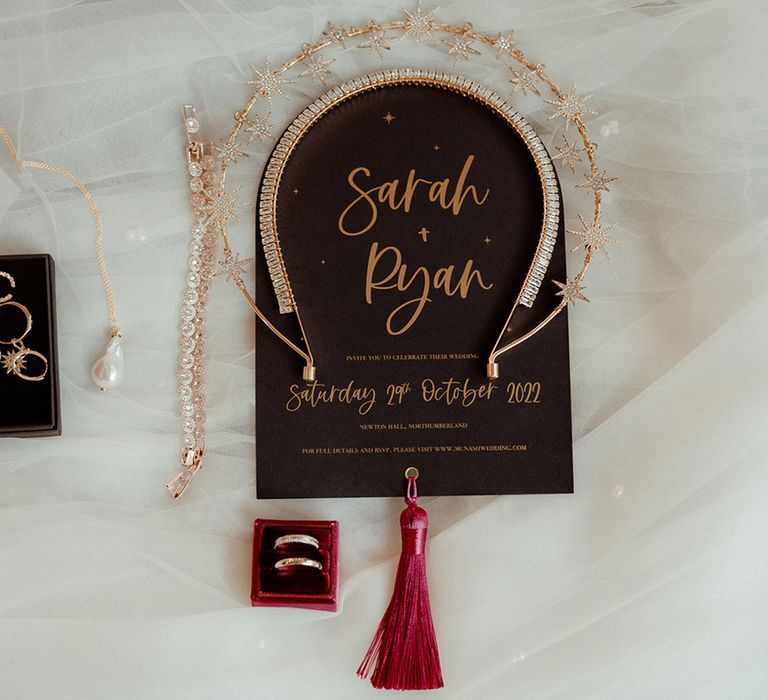 Black and gold wedding stationery with red tassel with the gold bridal crown, necklace, earrings and wedding rings in red velvet box