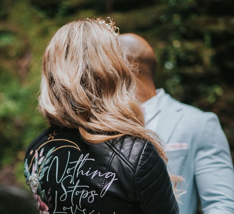 Bride in Painted Love wedding leather jacket with motif and the date of the wedding on with the groom in light blue suit 