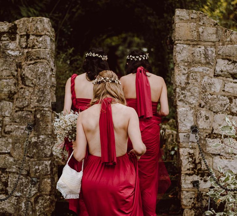 Bridesmaids in red satin halterneck bridesmaid dresses walking through The Orangery Maidstone wedding venue