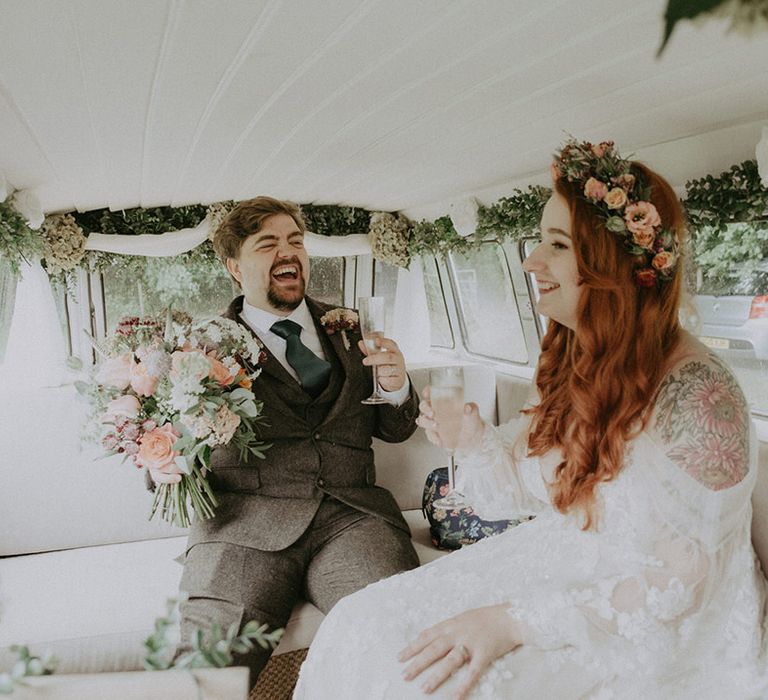 The groom in a three piece suit with the bride in a boho wedding dress with flower crown ride in the VW camper van wedding transport decorated with flowers