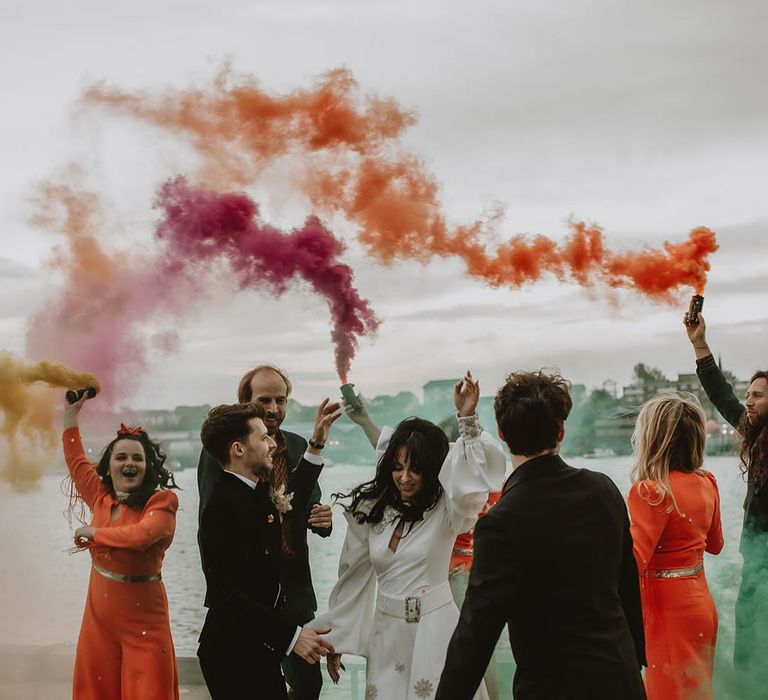 The wedding party all have fun together waving colourful smoke bombs around for colourful autumn wedding in the North East 