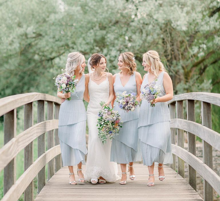 Light blue ruffle layered bridesmaid dresses walking along a bridge with the bride for pretty wedding photo 