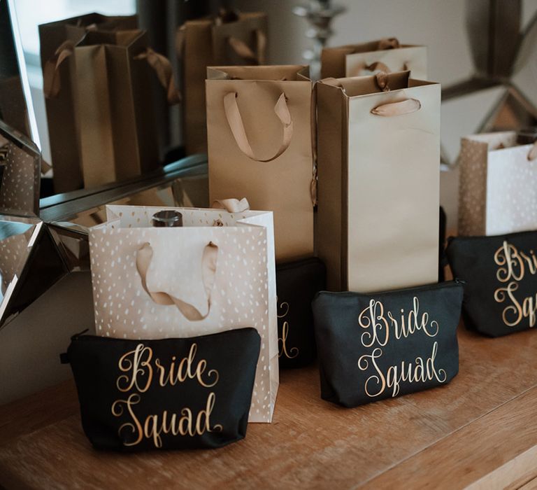 Gold gift bags for the bridal party with custom black makeup bags with gold writing reading 'bride squad' 