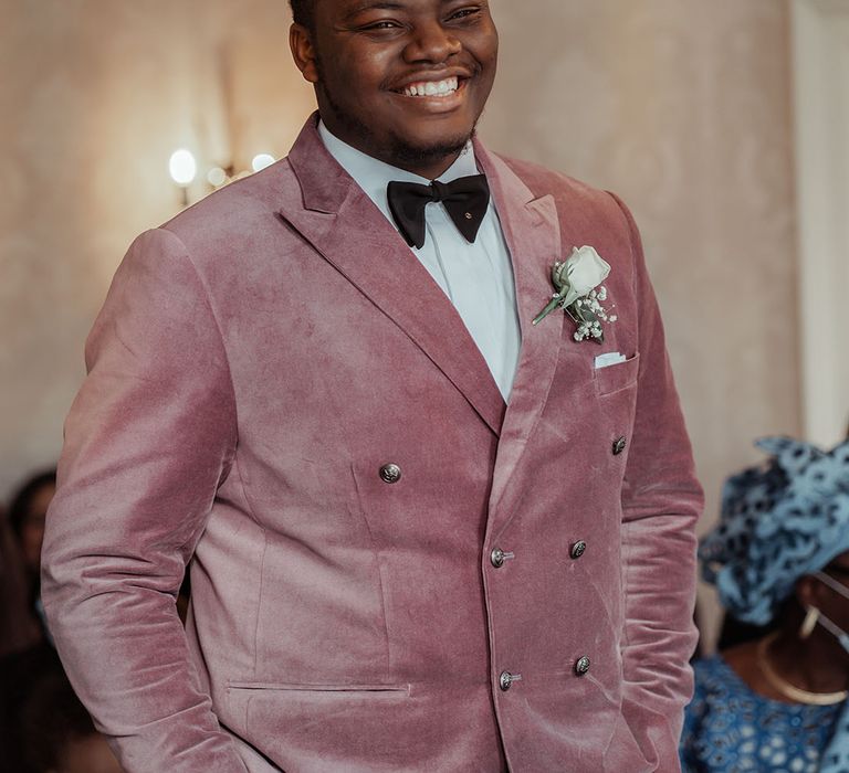 Groom in dusty pink double breasted velvet groom suit with black bow tie