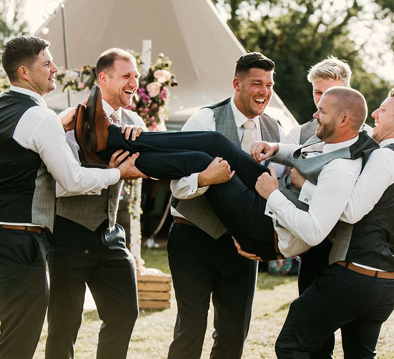 Groomsmen lift the groom up and pose for funny wedding photo 