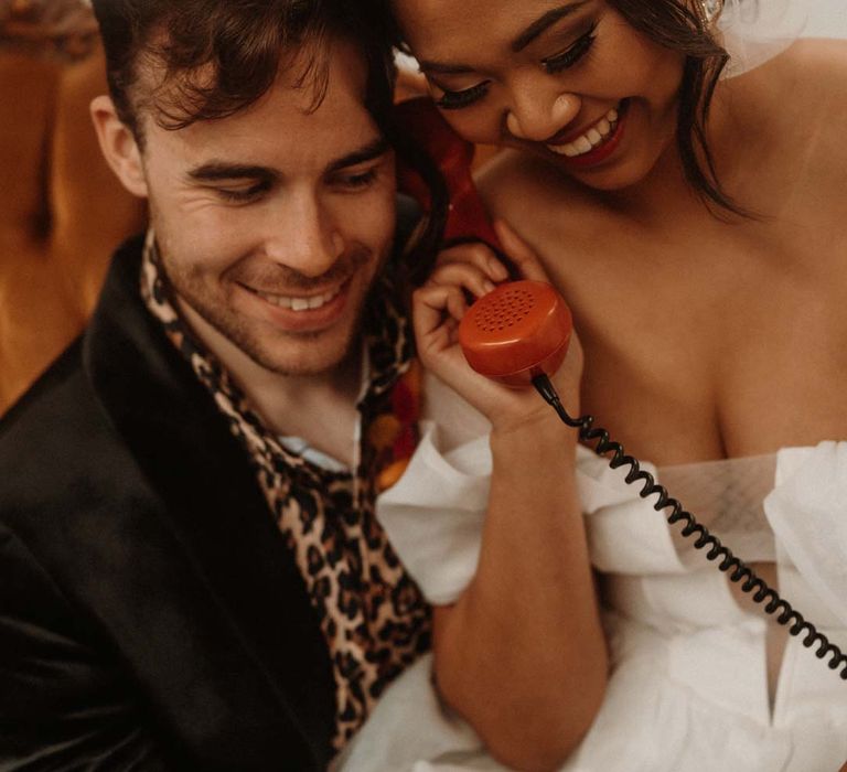 Bride in off shoulder tulle short wedding dress and groom in wet look black grooms suit with leopard print shirt doing wedding audio guest book 