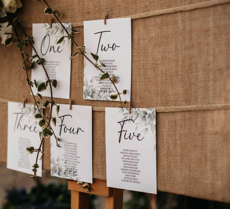 Botanical wedding seating plan in white and green with ivy on cork board 