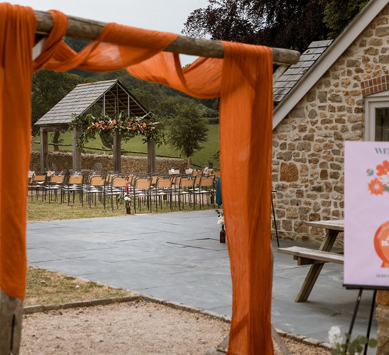 Orange drapery decorating the outdoor wedding ceremony with retro wedding welcome sign 