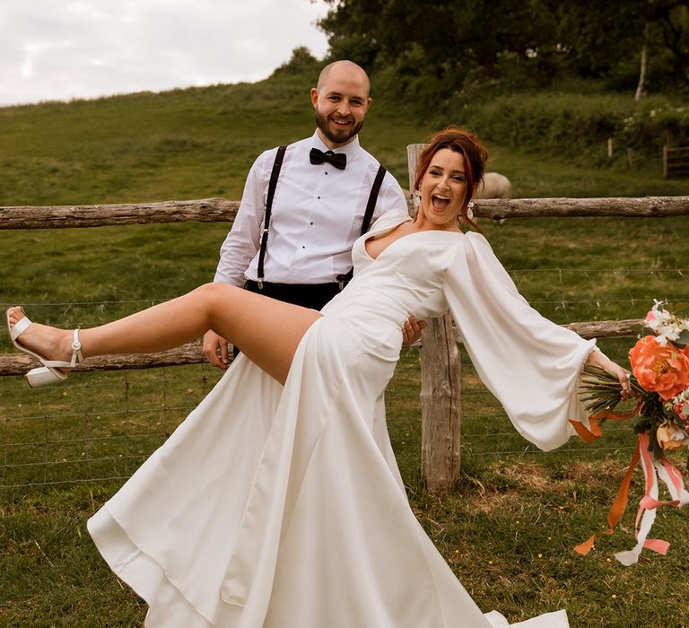 Bride in satin balloon sleeve wedding dress with front slit posing with groom in black tie 