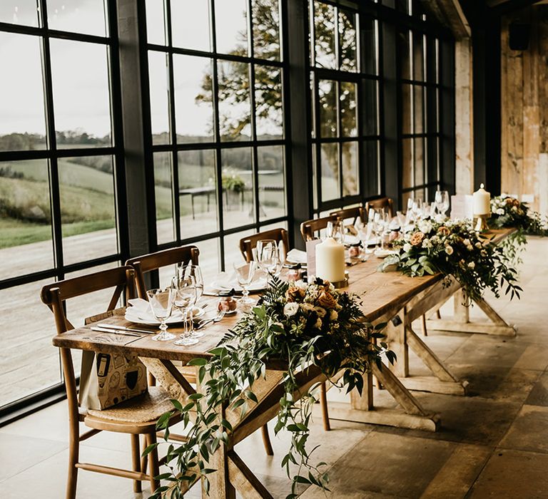 Foliage, orange and white wedding flowers, and pillar candles decorate the top table 