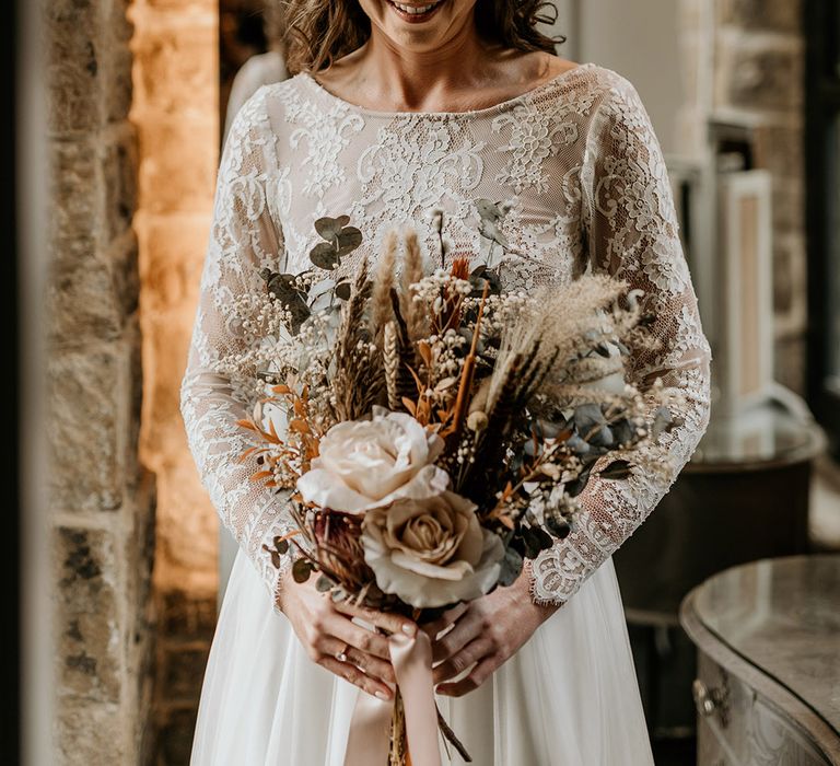 Bride wearing boho flower crown in long sleeve lace wedding dress carrying dried flower bouquet 