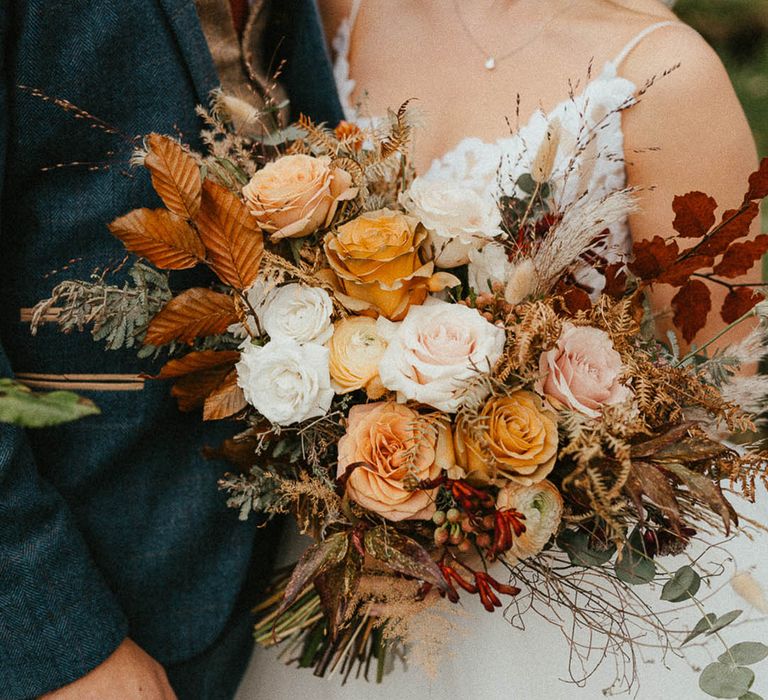 Bride carrying autumnal wedding bouquet with actual autumn leaves 