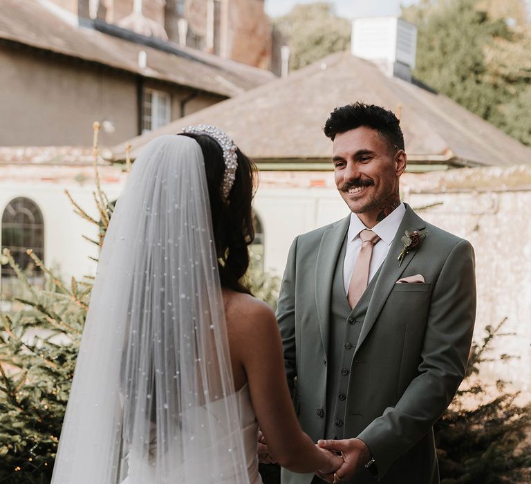 Bride wearing a pearl wedding veil smiling with the groom at their outdoor wedding ceremony 