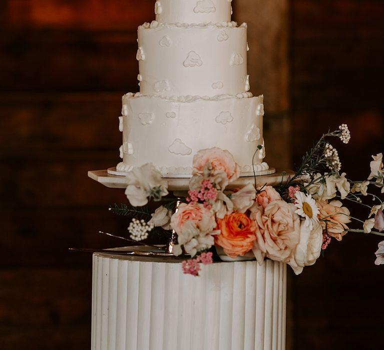 Three tier white frosted wedding cake with clouds iced on and custom cake toppers 