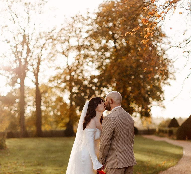 Groom in checkered suit kisses the bride in a bespoke wedding dress