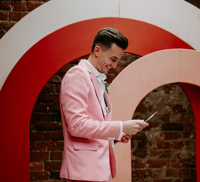 Groom in pink wedding suit reads wedding vows to the bride at the wedding ceremony 