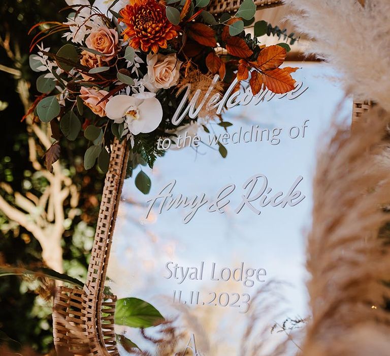 Mirror wedding welcome signage with orange and white wedding flowers with pampas grass decorations 