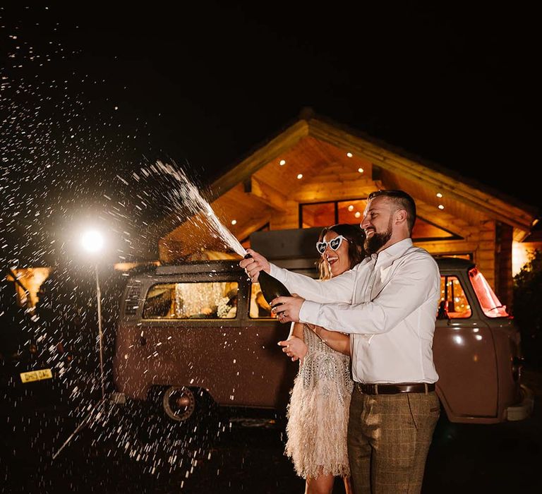 Champagne pop moment for bride and groom at wedding with bride wearing jewelled feather short wedding reception dress 