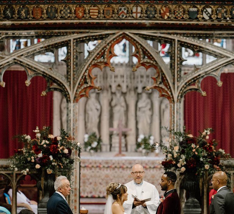 The bride and groom at their traditional Christian church wedding ceremony with groom in red velvet tuxedo 