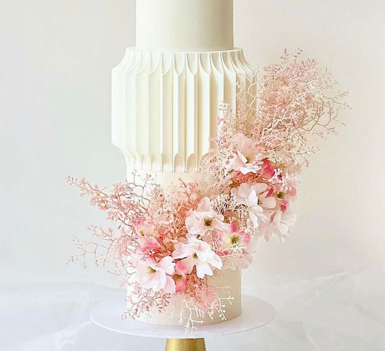 Unique white iced wedding cake with unusual shape decorated with light pale pink flowers 