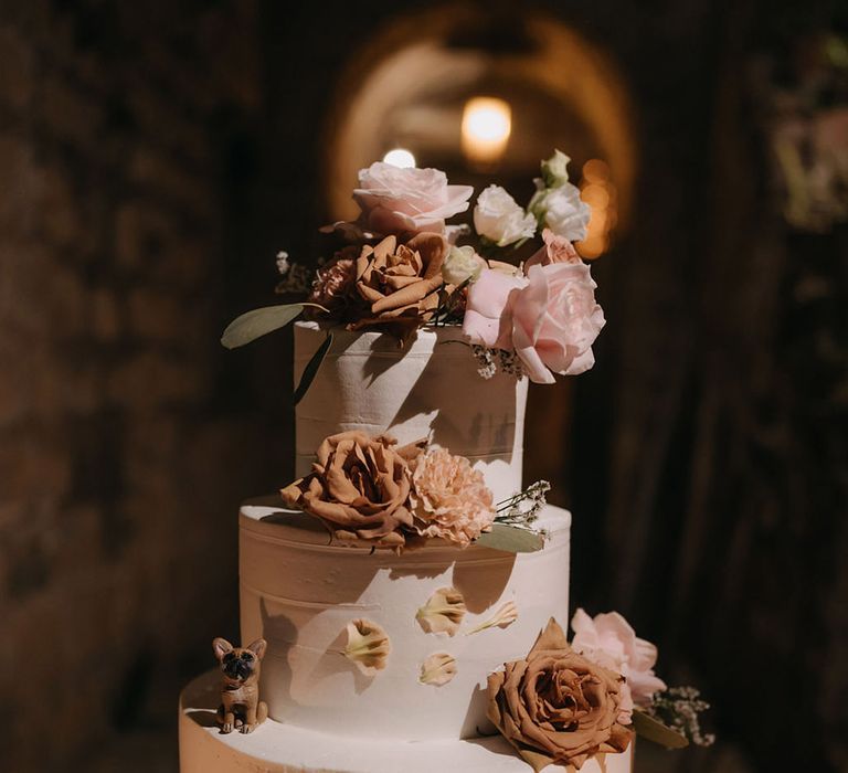 Three tier white iced wedding cake decorated with toffee roses and mini dog figure 