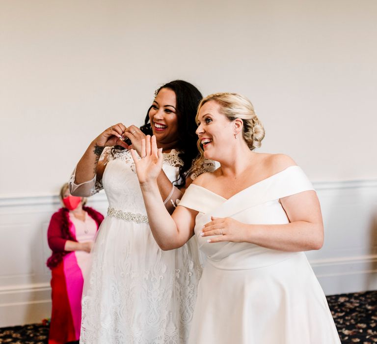 Newly-wed lesbian couple making heart signs on their wedding day 