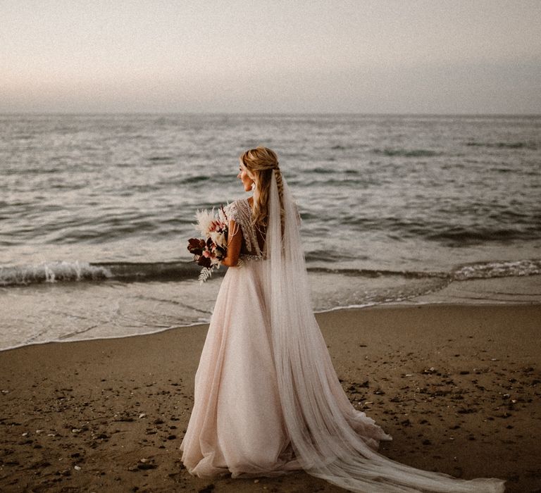 Bride on the beach with her bouquet and long cathedral length veil