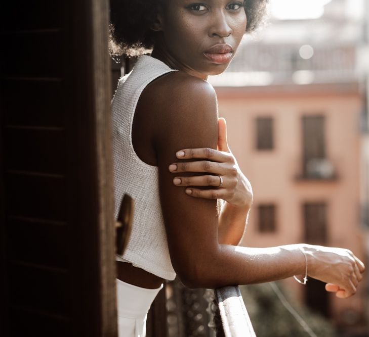 Bride stood on balcony in white trousers and top 