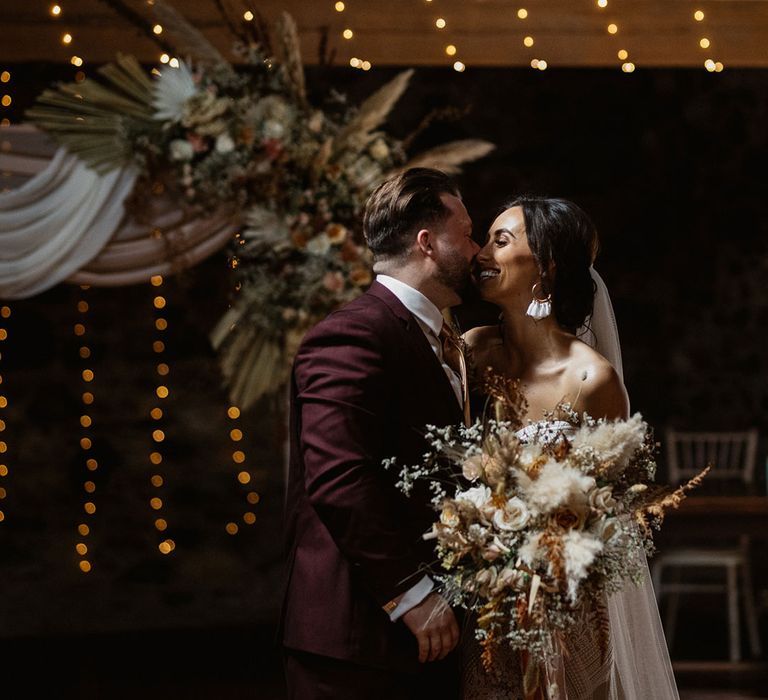 Groom kissing bride holding pampas grass and gypsophila bouquet 