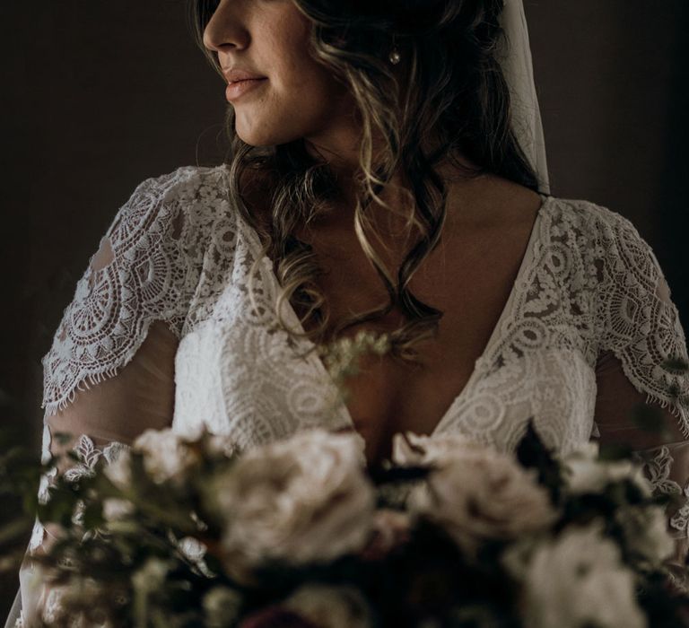 Bride with rose flower crown and v neck boho bridal dress holding rose bouquet looks to her right out the window