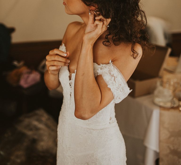 Bride with brown curly hair putting on pearl earrings 