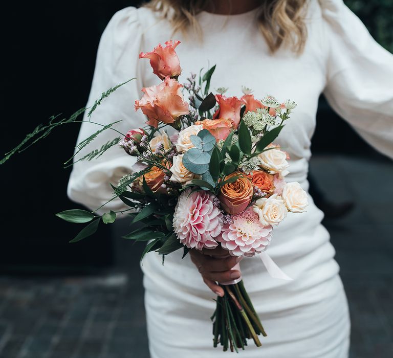 Bride wearing short wedding dress holding pink and coral bouquet with roses 