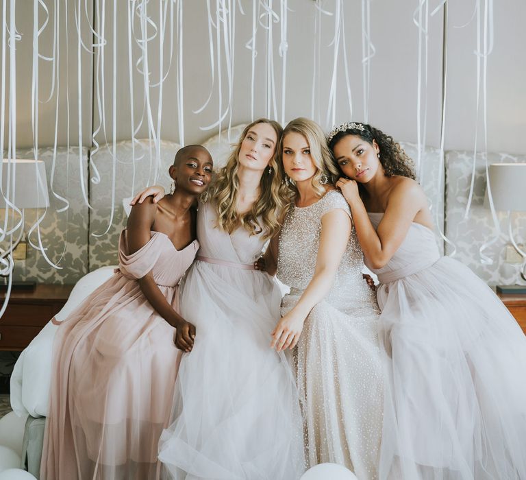 Bride in sparkly separates and bridesmaids in chiffon TH&TH dresses on the wedding morning with white and gold balloon ceiling backdrop 